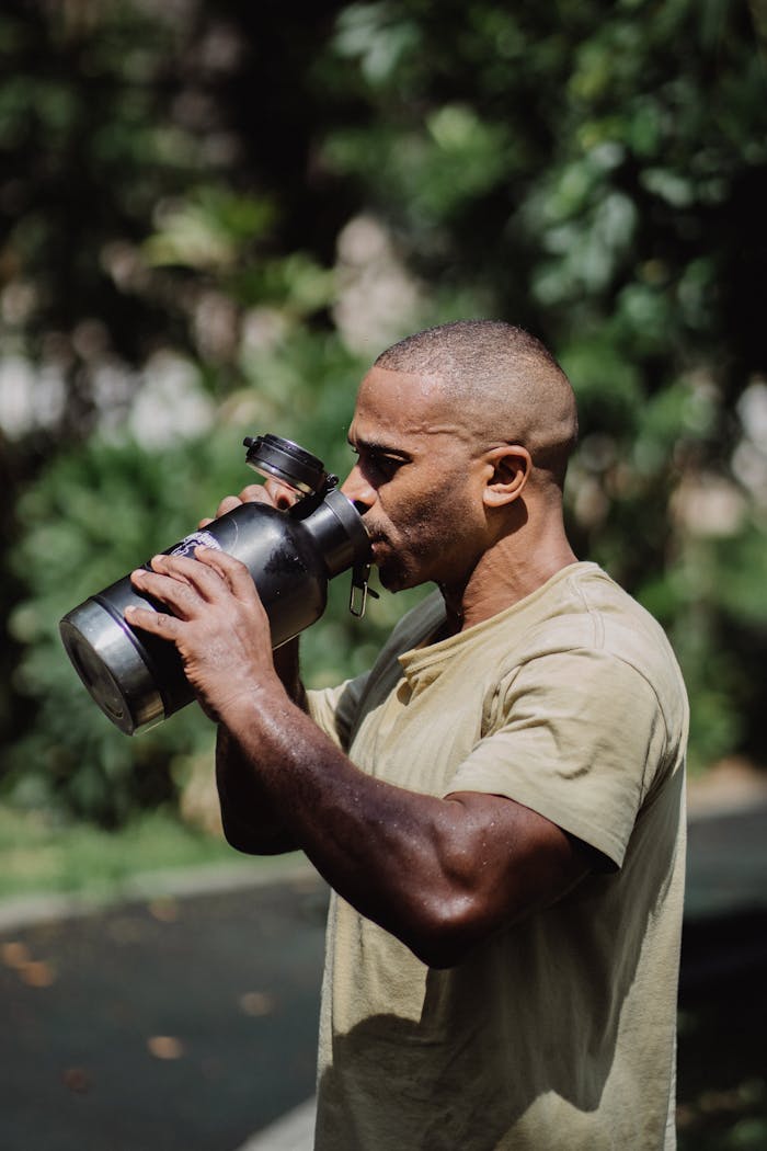 Athletic man drinking water from a large tumbler outdoors, captured in a natural setting.