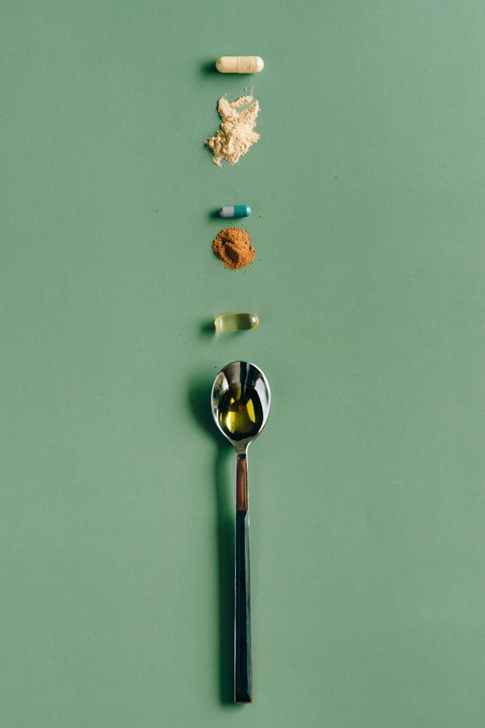 Assorted supplements and a spoon laid out on a green surface, showcasing health concepts.